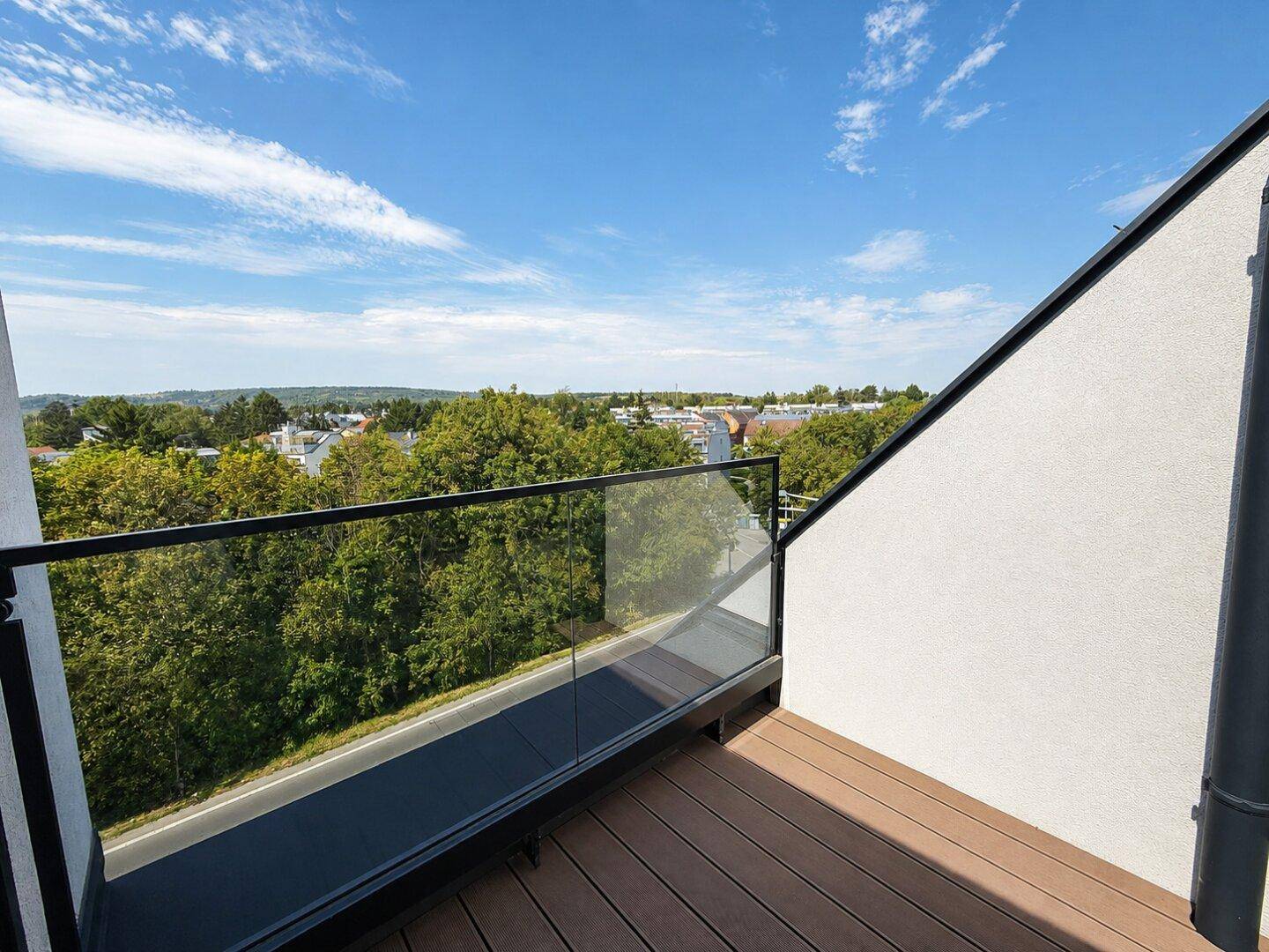 Balkon mit Glasgeländer und weitem Blick ins Grüne und auf die umliegende Bebauung.