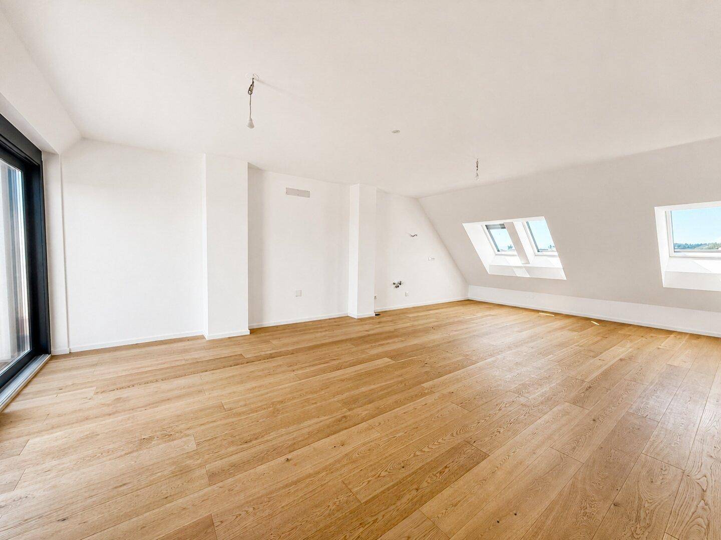 Heller, leerer Raum mit Holzboden, Dachschrägen und mehreren Dachfenstern für viel Licht.