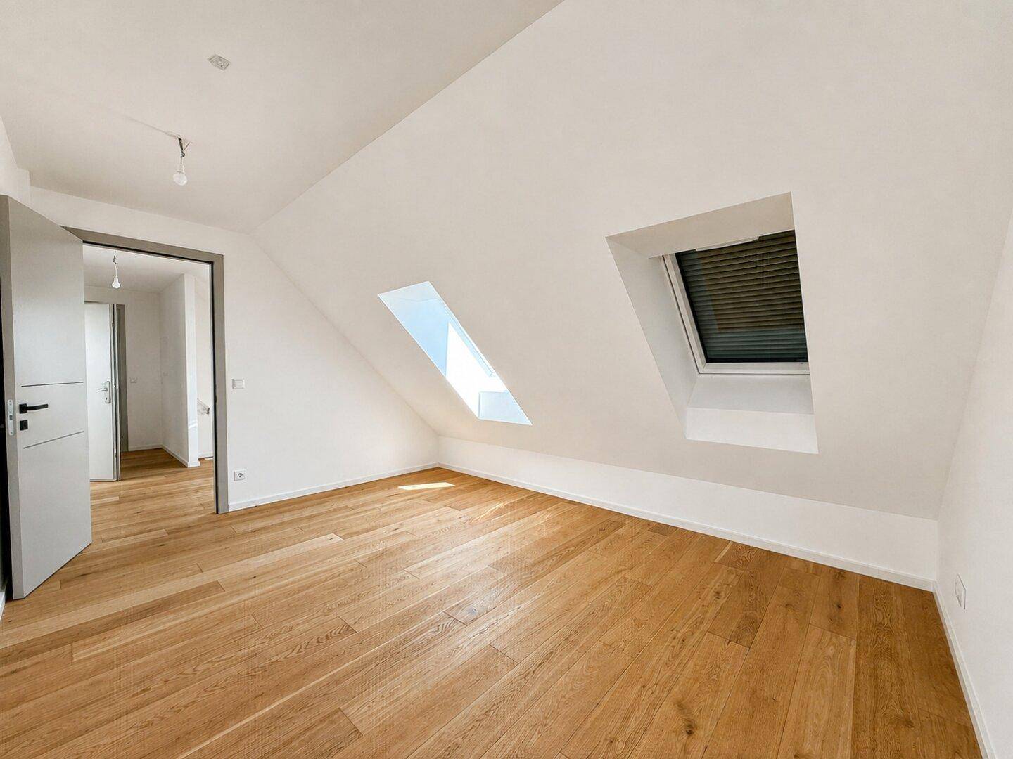 Leeres Zimmer mit Holzboden, Dachschrägen und zwei Dachfenstern, ideal als Schlafzimmer.
