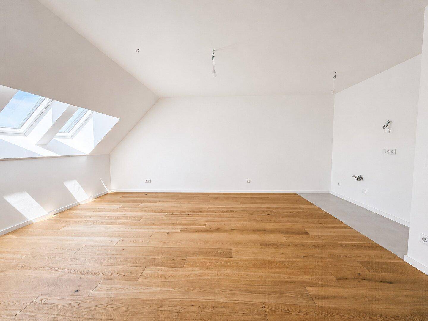 Leeres, lichtdurchflutetes Zimmer mit Holzboden, Dachschrägen und großen Dachfenstern.