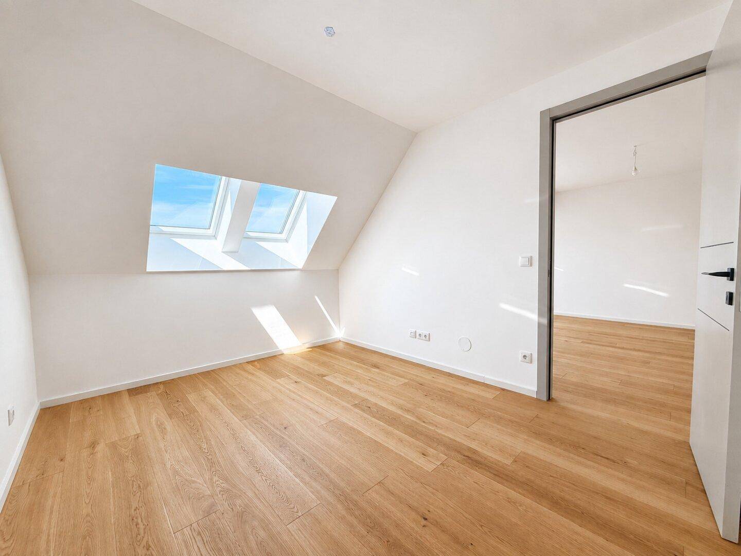 Unmöbliertes Schlafzimmer mit Holzboden, Dachschrägen, Dachfenstern und offener Tür.