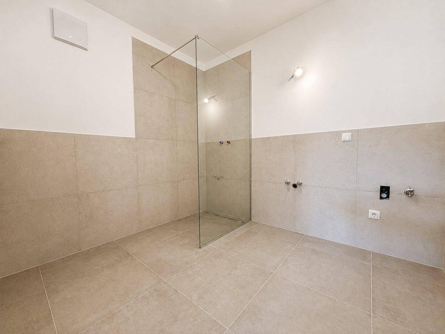 Modernes Badezimmer mit beigefarbenen Fliesen und einer geräumigen begehbaren Dusche.