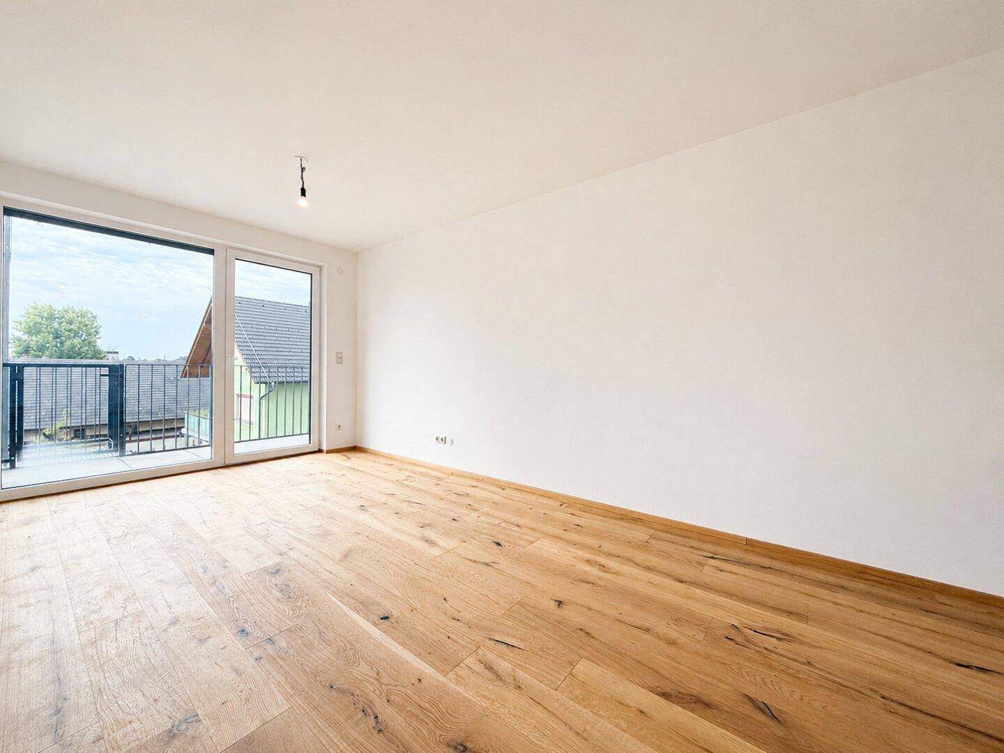 Geräumiger, heller Raum mit Holzboden und direktem Zugang zu einem Balkon.