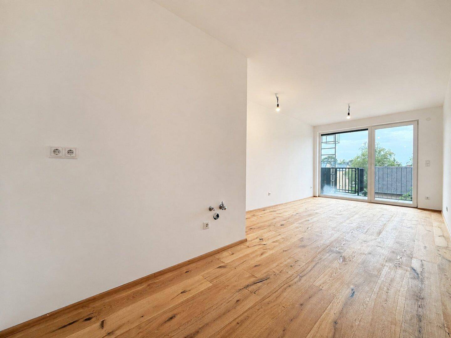 Heller Raum mit Holzboden und Balkonzugang, vorbereitet für eine moderne Küche.