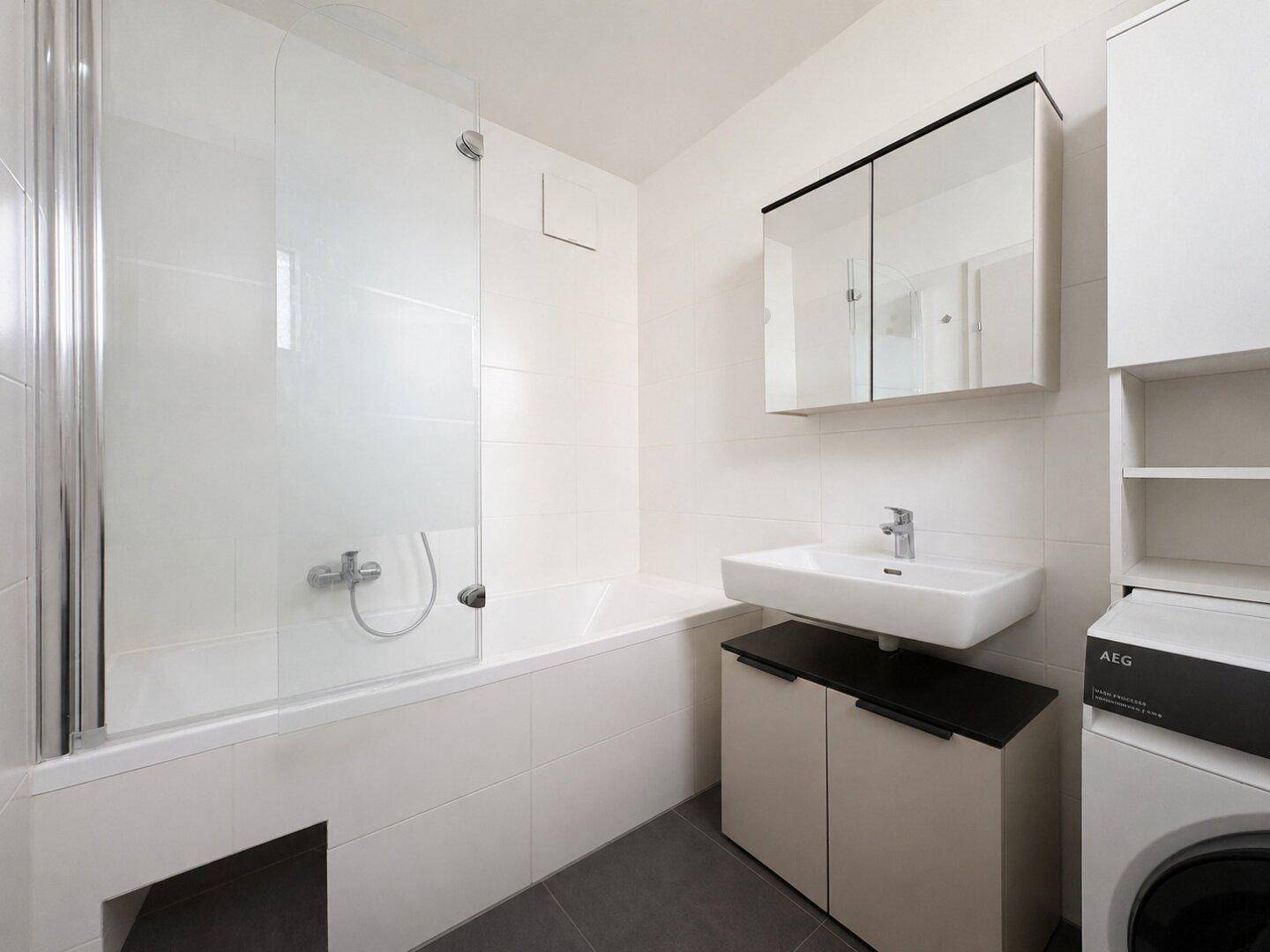 Modernes Badezimmer mit Badewanne, Waschbecken, Spiegelschrank und Waschmaschine.