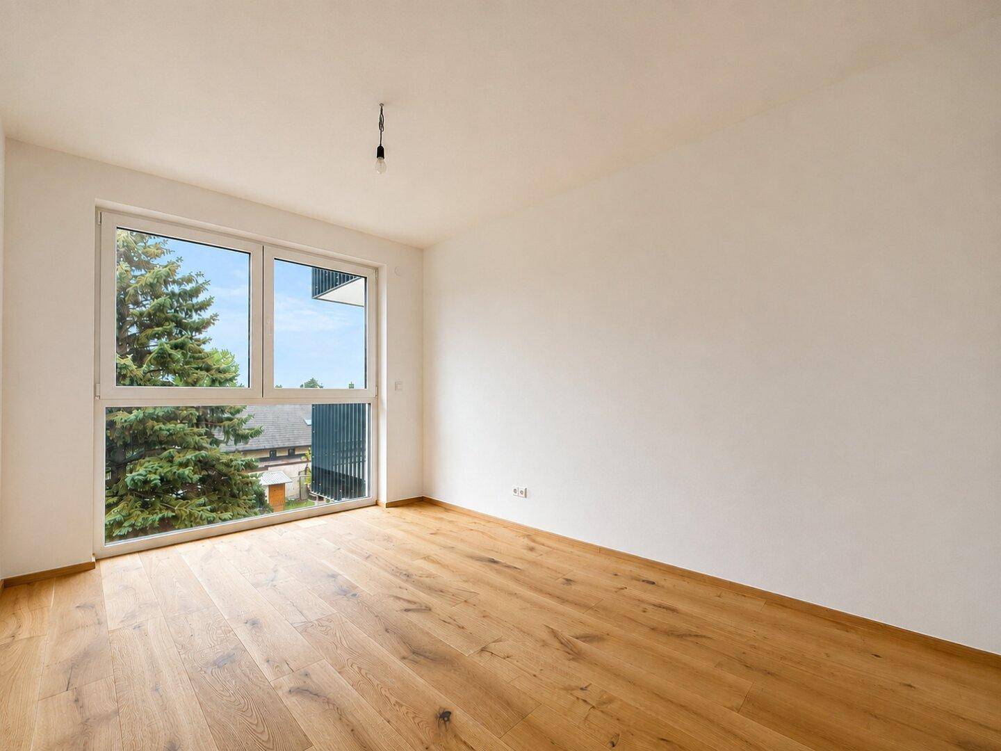 Unmöbliertes Zimmer mit Holzboden und großem Fenster, ideal als Schlaf- oder Arbeitszimmer.