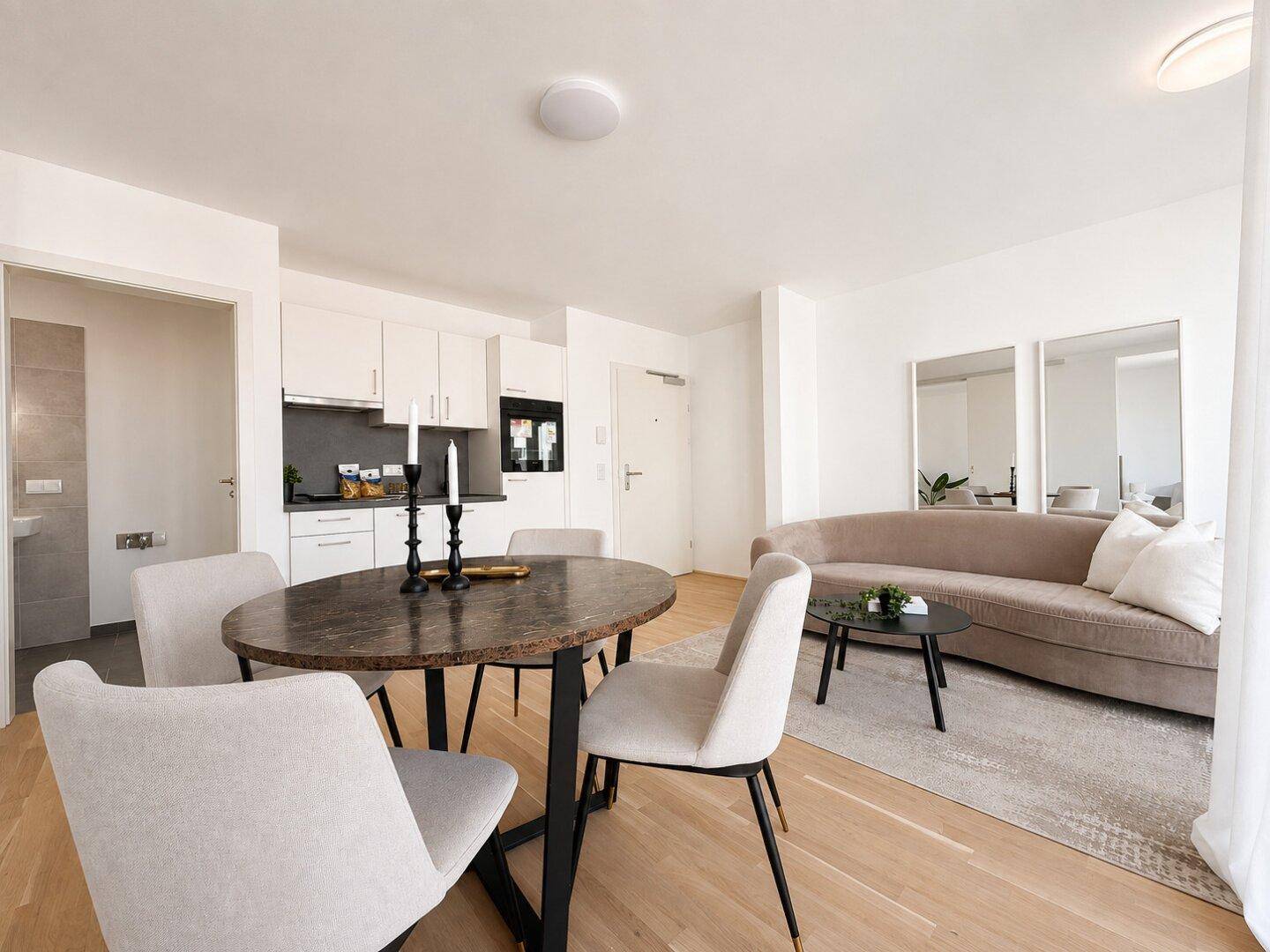 Offener Wohnbereich mit integrierter Küche, Esstisch und beigem Sofa.