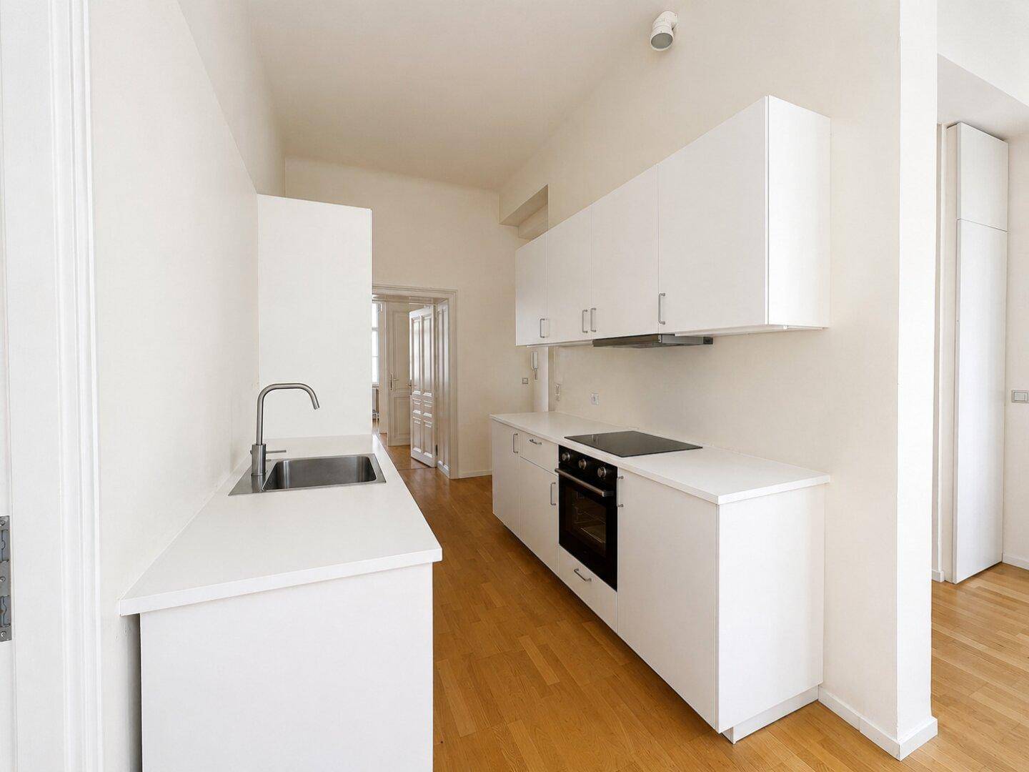 Moderne, helle Küche mit weißen Schränken, Induktionskochfeld und Backofen, ausgestattet mit Parkettboden.