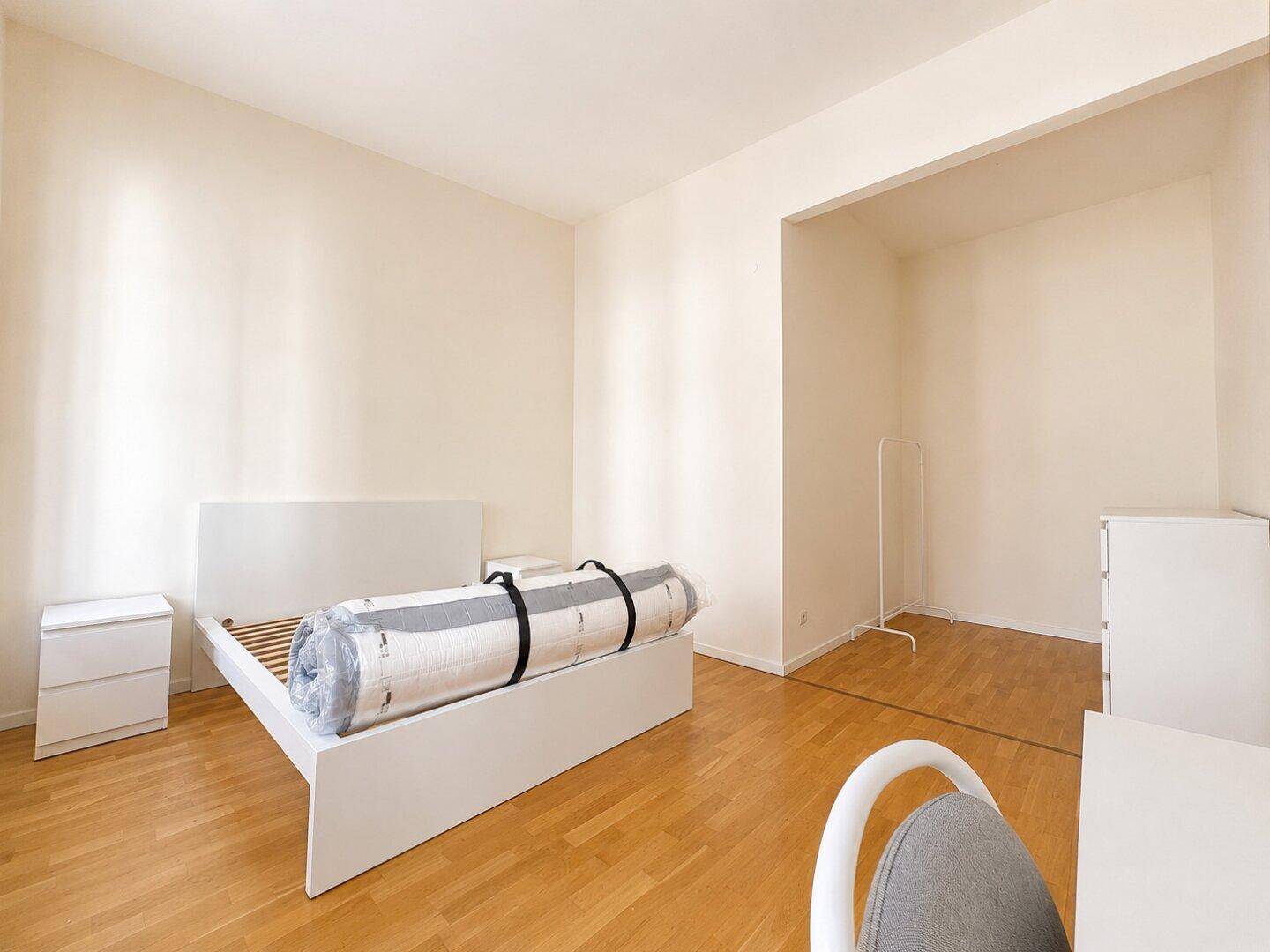 Helles Schlafzimmer mit Parkettboden und einem Alkoven, ideal für einen begehbaren Kleiderschrank.
