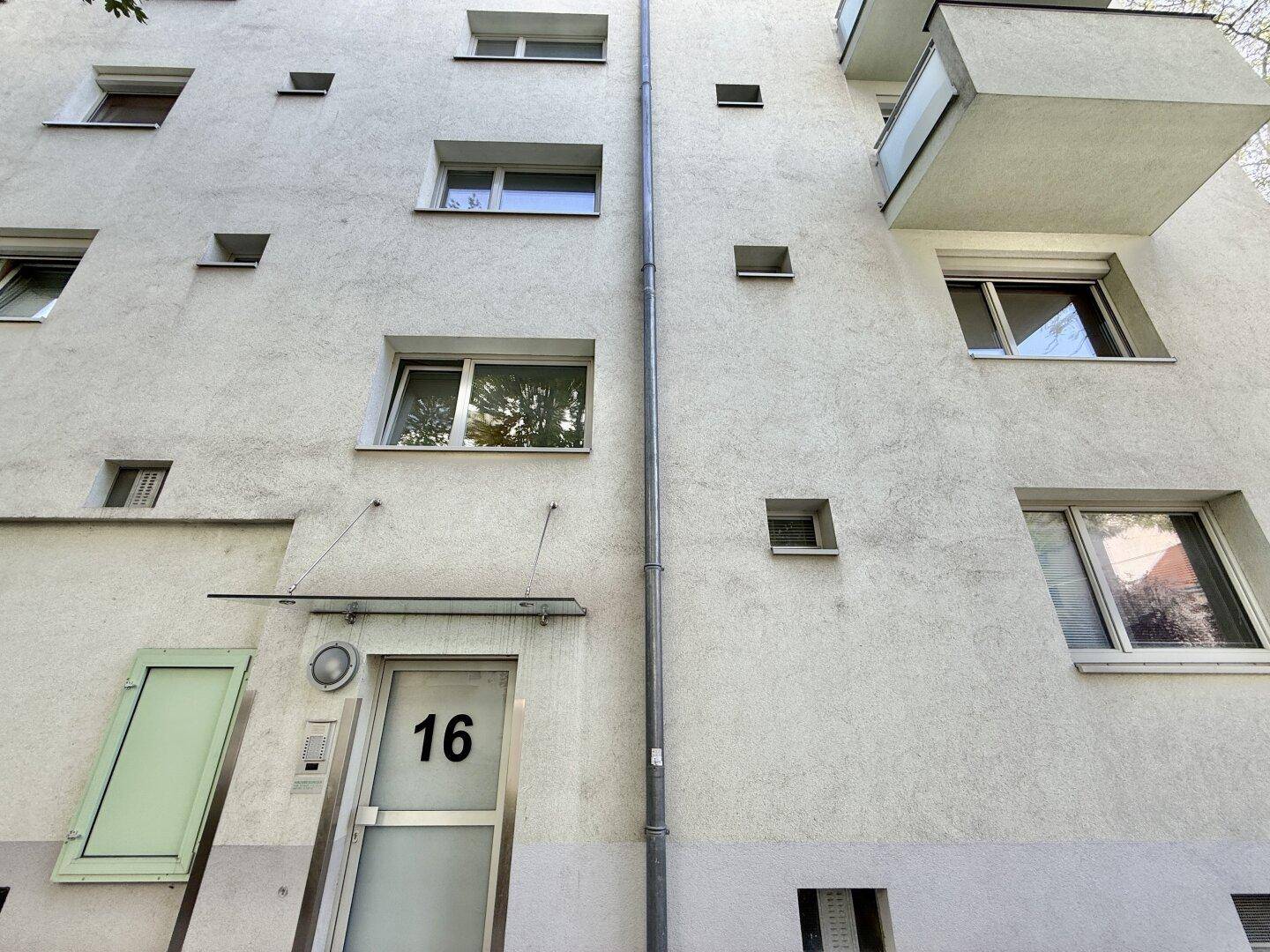 Fassade eines Mehrfamilienhauses mit mehreren Fenstern und einem Balkon, der eine moderne Architektur aufweist.