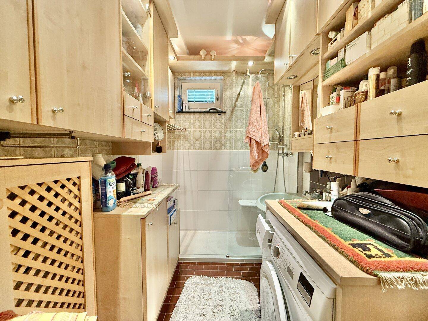Schmales Badezimmer mit Dusche, Waschmaschine und vielen Holzschränken für Stauraum, praktisch und funktional gestaltet.