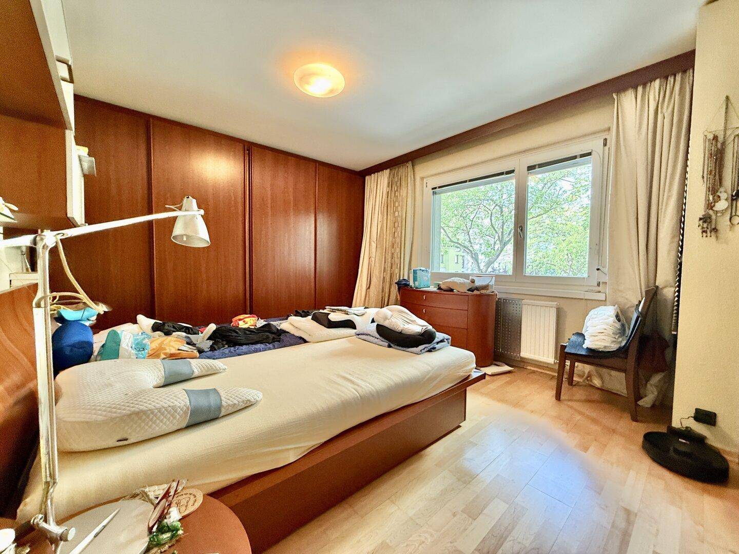 Schlafzimmer mit Holzboden, Einbauschränken und großem Fenster mit Blick ins Grüne, das für viel Helligkeit sorgt.