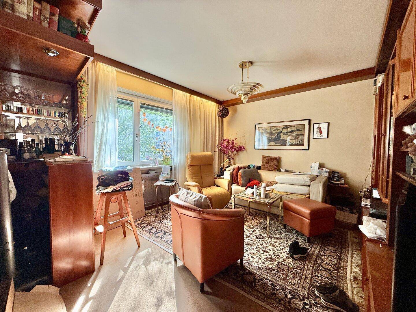 Wohnzimmer mit Teppichboden, Holzmöbeln und großem Fenster, das viel Tageslicht hereinlässt und eine angenehme Atmosphäre schafft.