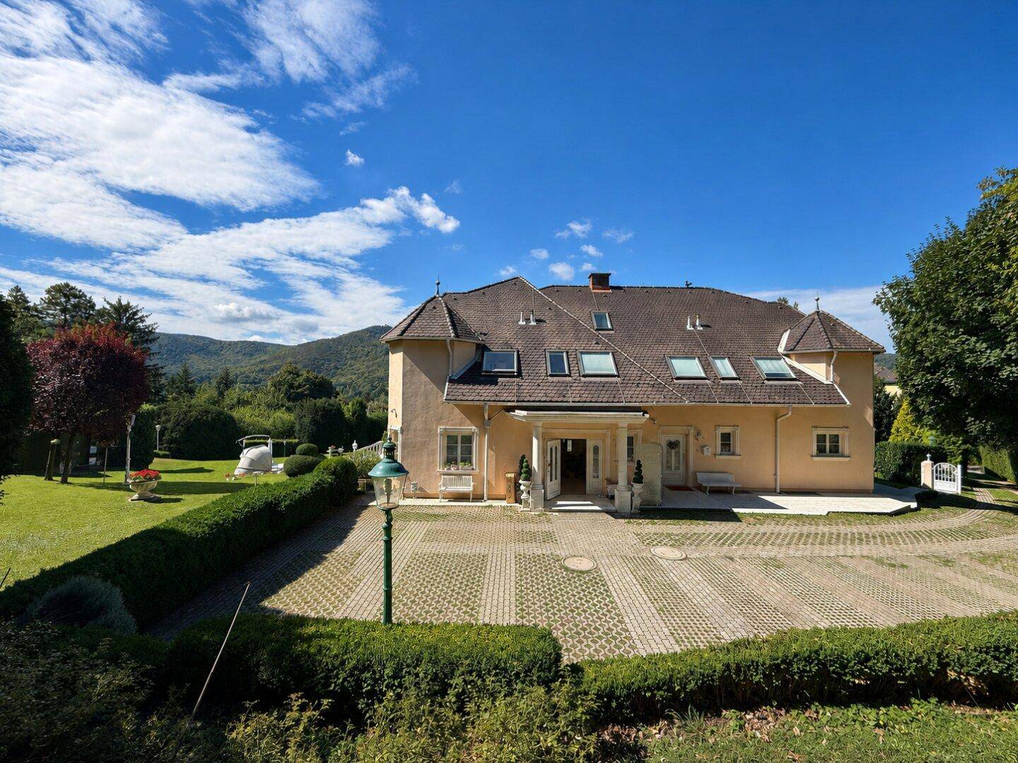 Vorderansicht des Hauses mit großzügiger gepflasterter Auffahrt und gepflegter Gartenanlage.