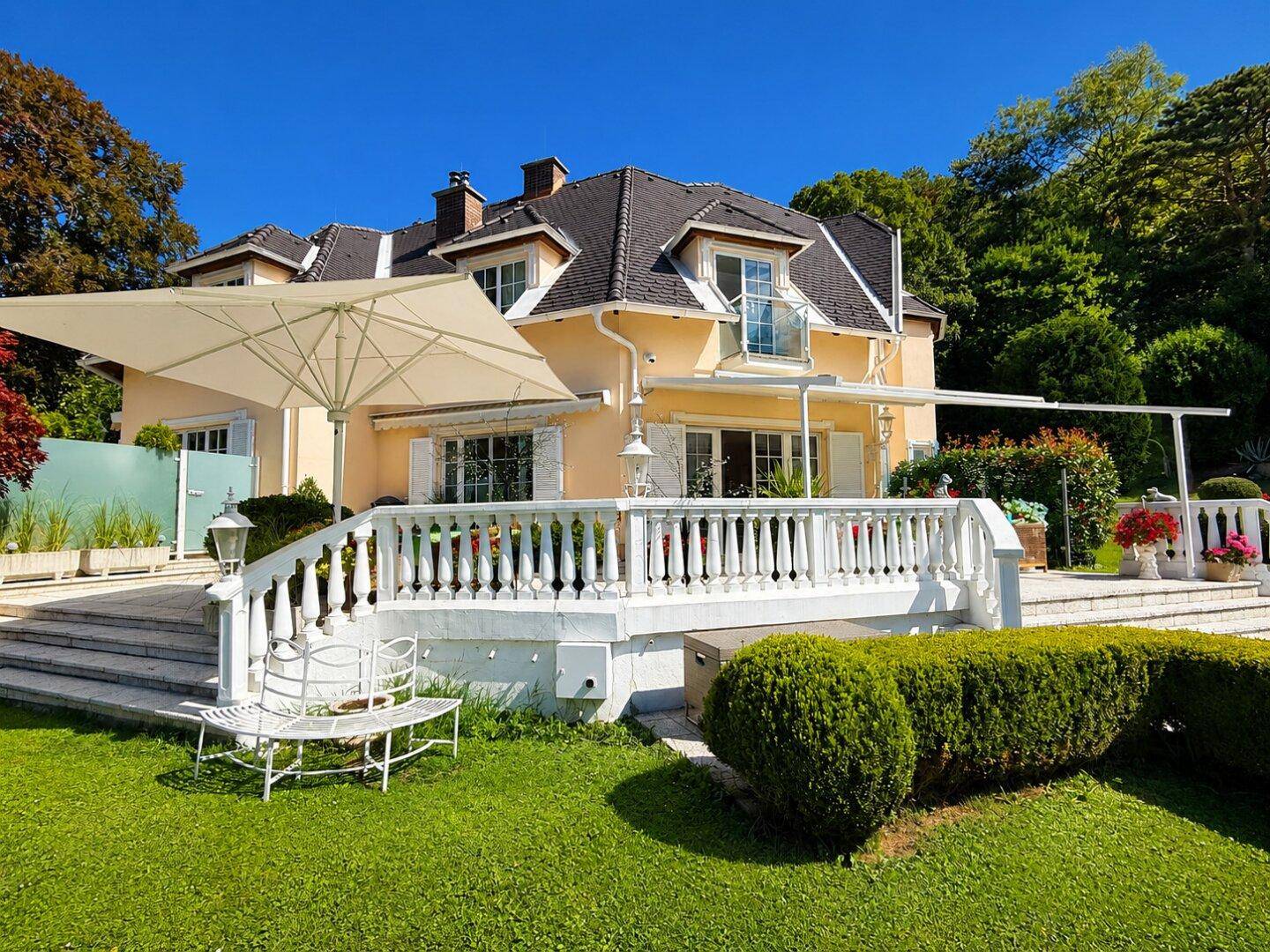 Seitenansicht des Hauses mit großer Terrasse, Sonnenschirm und weitläufigem Gartenbereich.