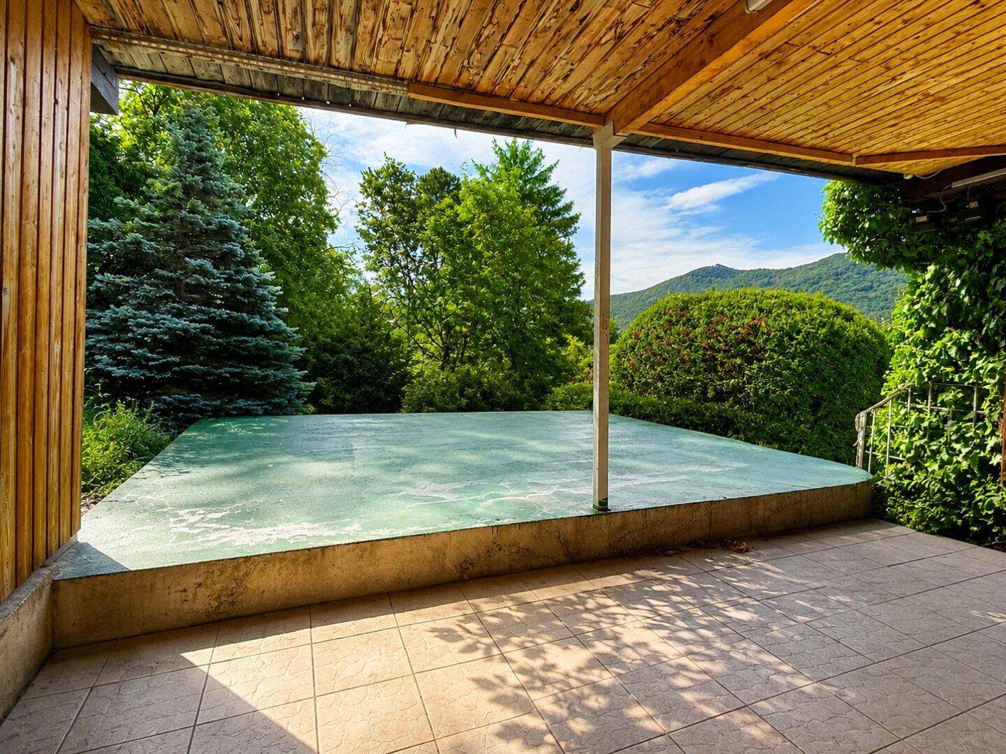 Überdachte Terrasse mit Fliesenboden und weitem Blick auf die grüne Umgebung und Berge.
