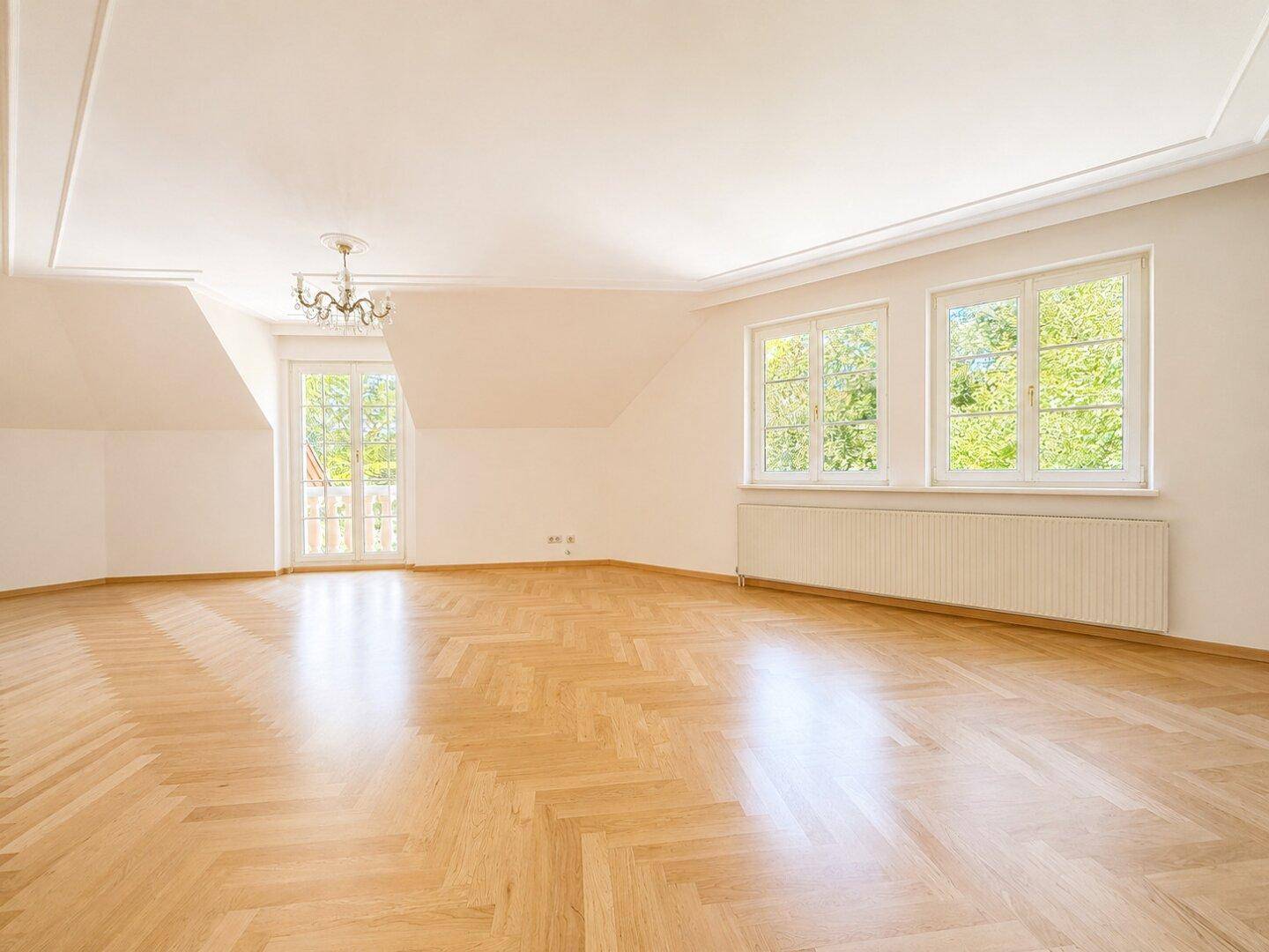 Geräumiges, leeres Schlafzimmer mit Fischgrätparkett und Zugang zu einem französischen Balkon.