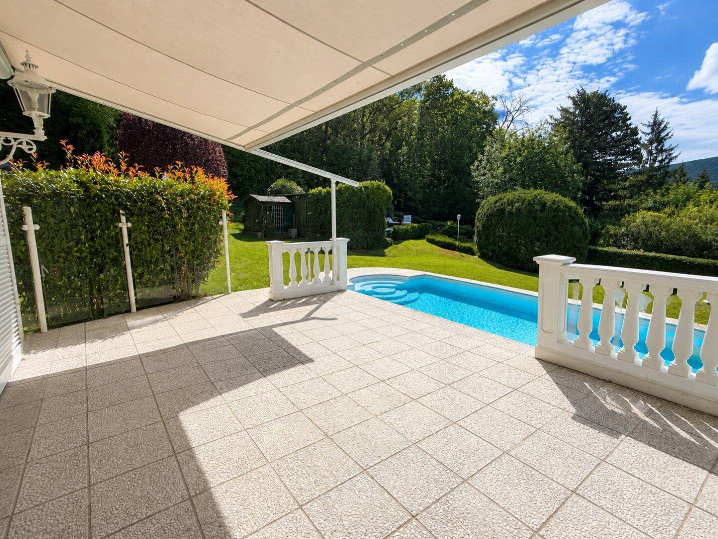 Geflieste Terrasse mit kleinem Pool, umgeben von Hecken und grüner Natur.
