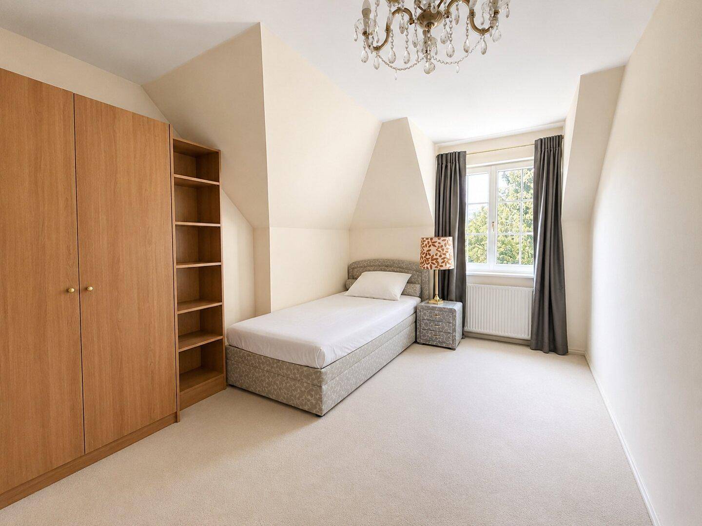 Gemütliches Schlafzimmer mit Teppichboden, Einzelbett und Kleiderschrank unter Dachschrägen.