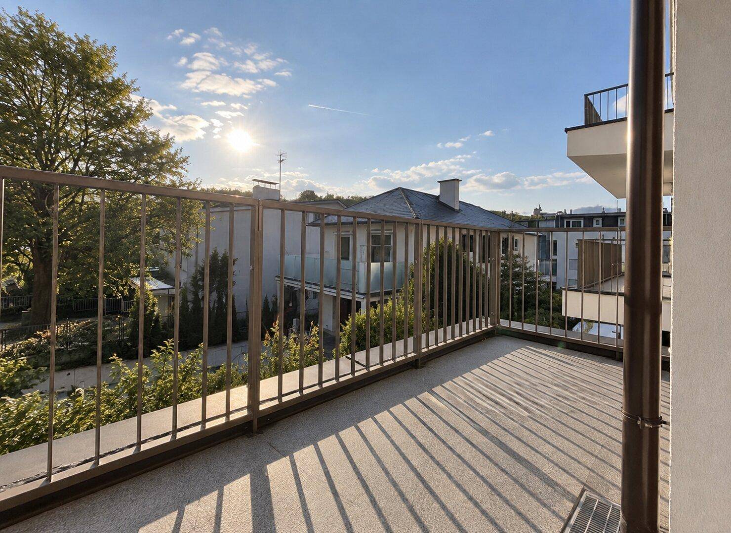 Leerer Balkon mit Metallgeländer, Fliesenboden und weitem Blick auf die Nachbarschaft.