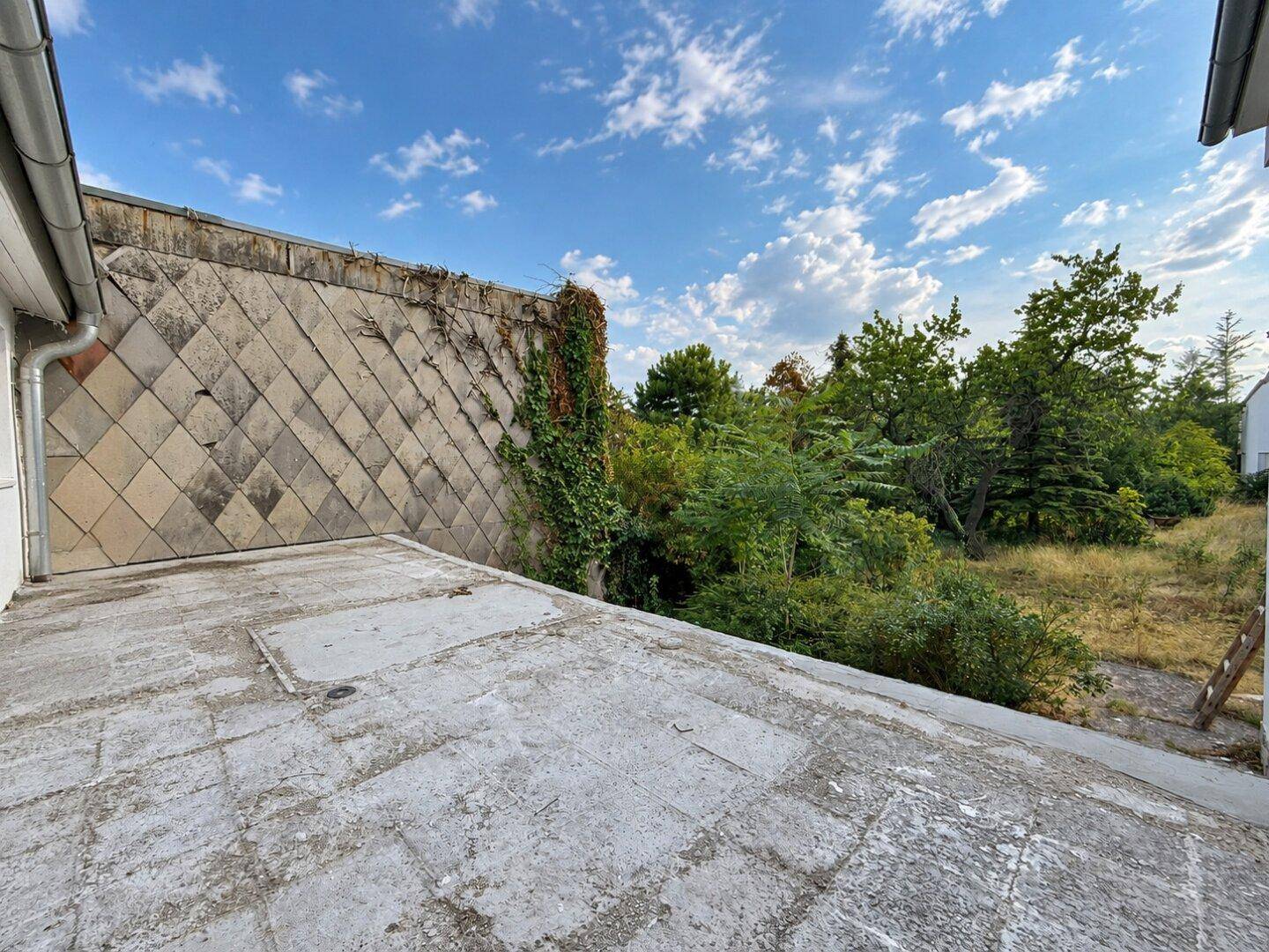 Ungepflegte Dachterrasse mit Blick auf üppiges Grün und bewölkten Himmel.