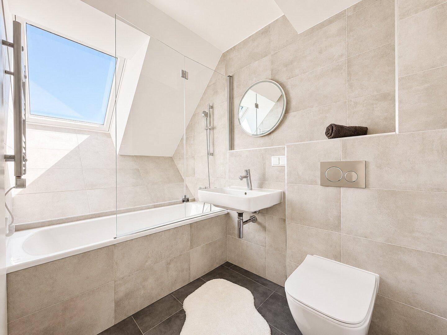 Modernes Badezimmer mit hellen Fliesen, Badewanne mit Duschfunktion und einem Dachfenster.