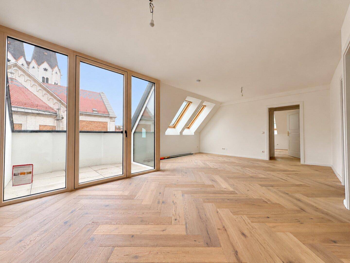 Heller, unmöblierter Raum mit Fischgrätparkett, Dachschrägen und Blick auf die Kirchtürme.