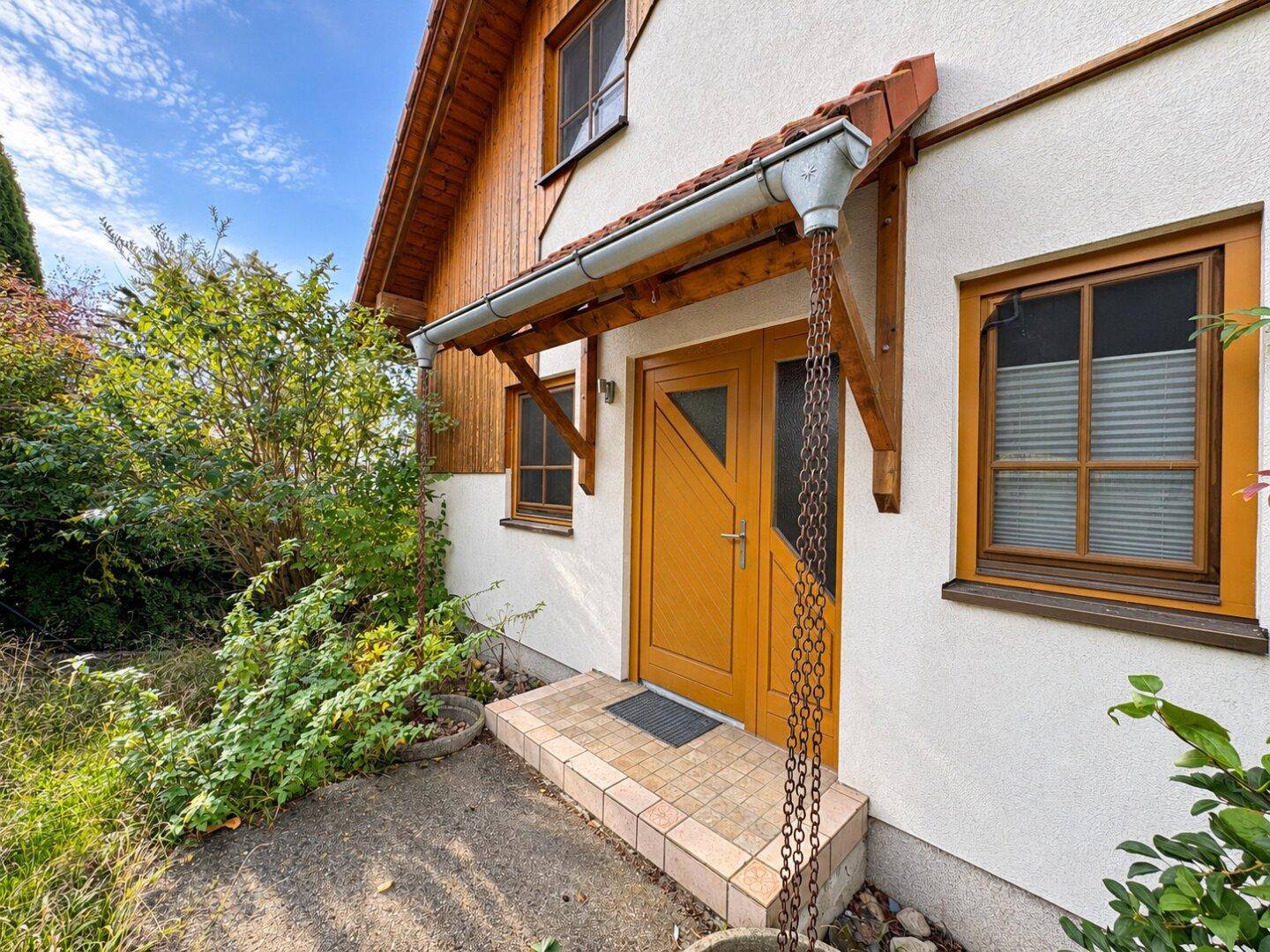 Eingangsbereich des Hauses mit Holztür, Vordach und gepflegter Umgebung.