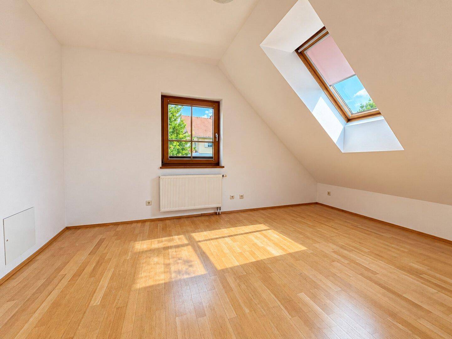 Helles Schlafzimmer mit Parkettboden, Dachschräge und zusätzlichem Dachfenster.