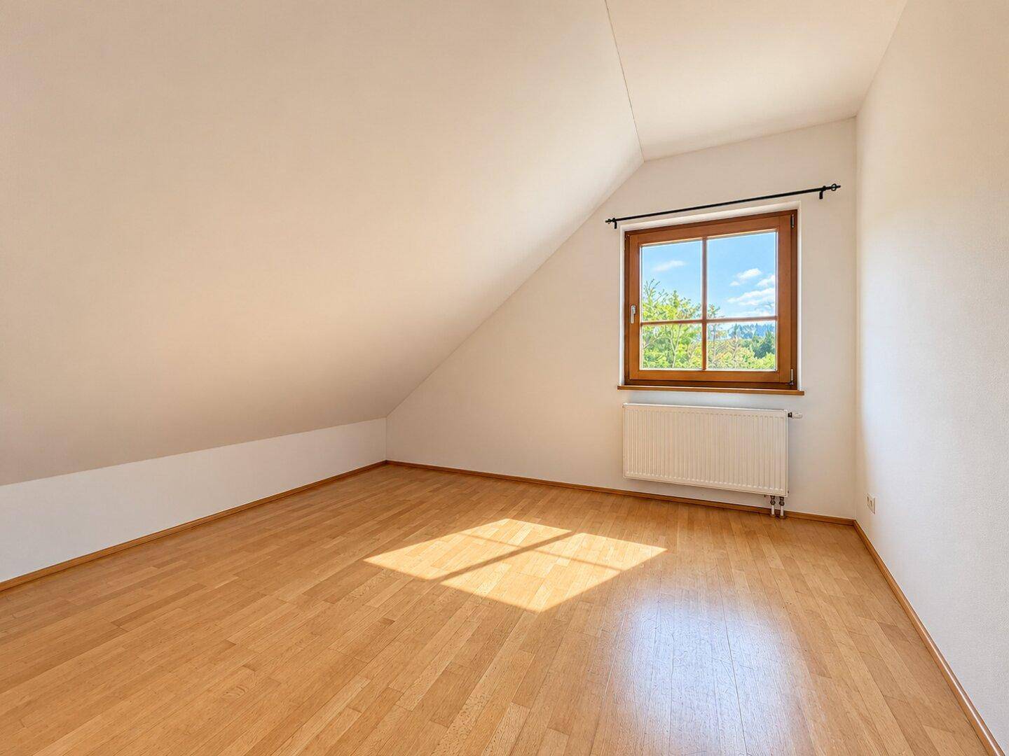 Gemütliches Schlafzimmer mit Parkettboden, Dachschräge und Fenster mit Ausblick.