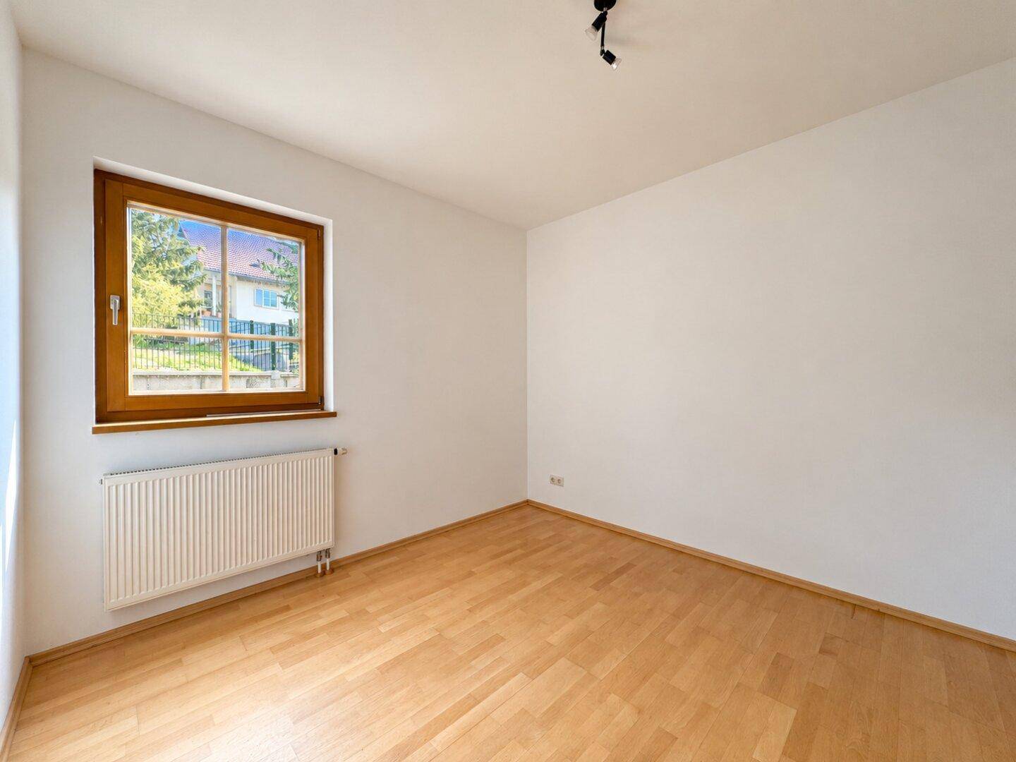 Helles Schlafzimmer mit Parkettboden und Fenster, bereit zur individuellen Gestaltung.