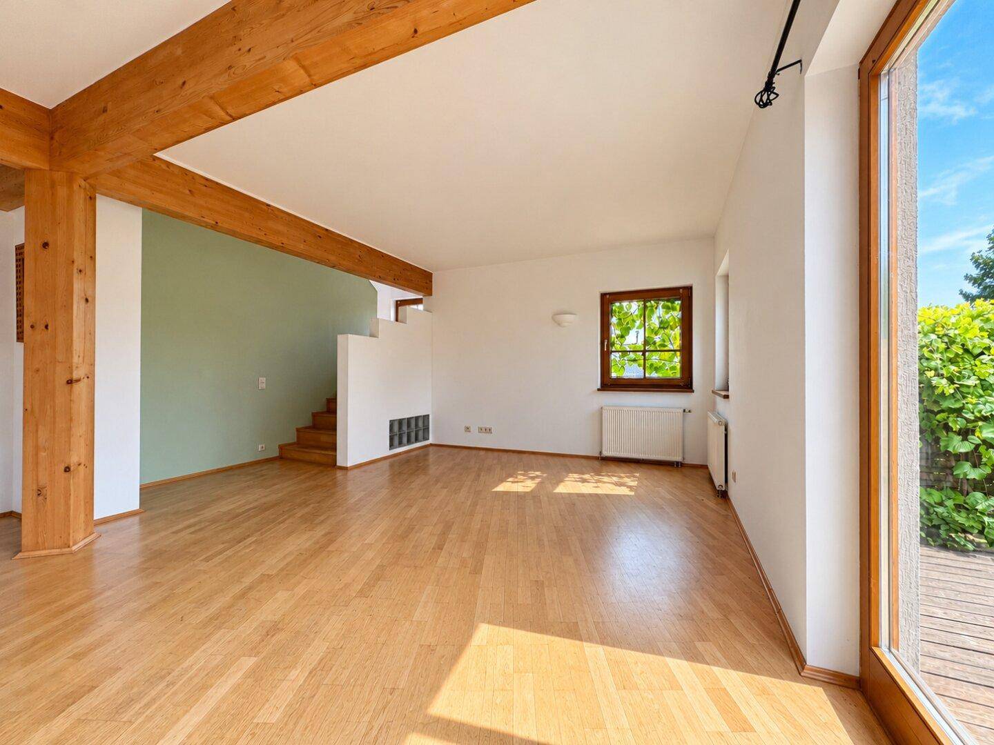 Geräumiges Wohnzimmer mit Holzbalken, Parkettboden und viel Tageslicht.