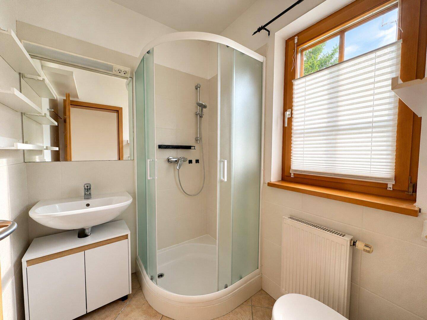Kleines Badezimmer mit Duschkabine, Waschbecken und Fenster für Tageslicht.