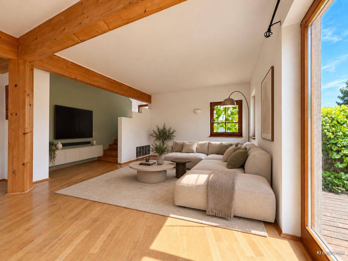 Modern eingerichtetes Wohnzimmer mit beigem Sofa, Holzbalken und Blick ins Grüne.
