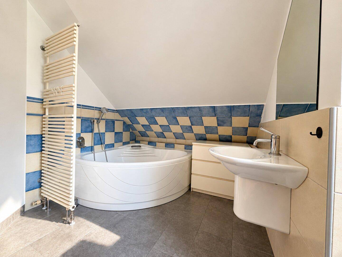 Badezimmer mit Eckbadewanne, beheiztem Handtuchhalter und farbigen Fliesen.