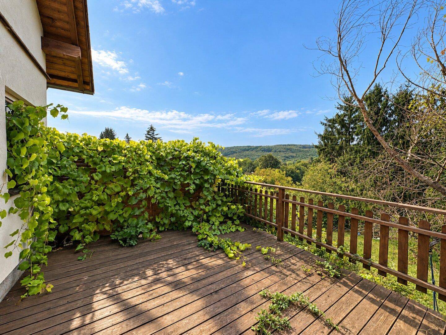 Holzterrasse mit üppigem Grün und weitem Blick über die Landschaft.