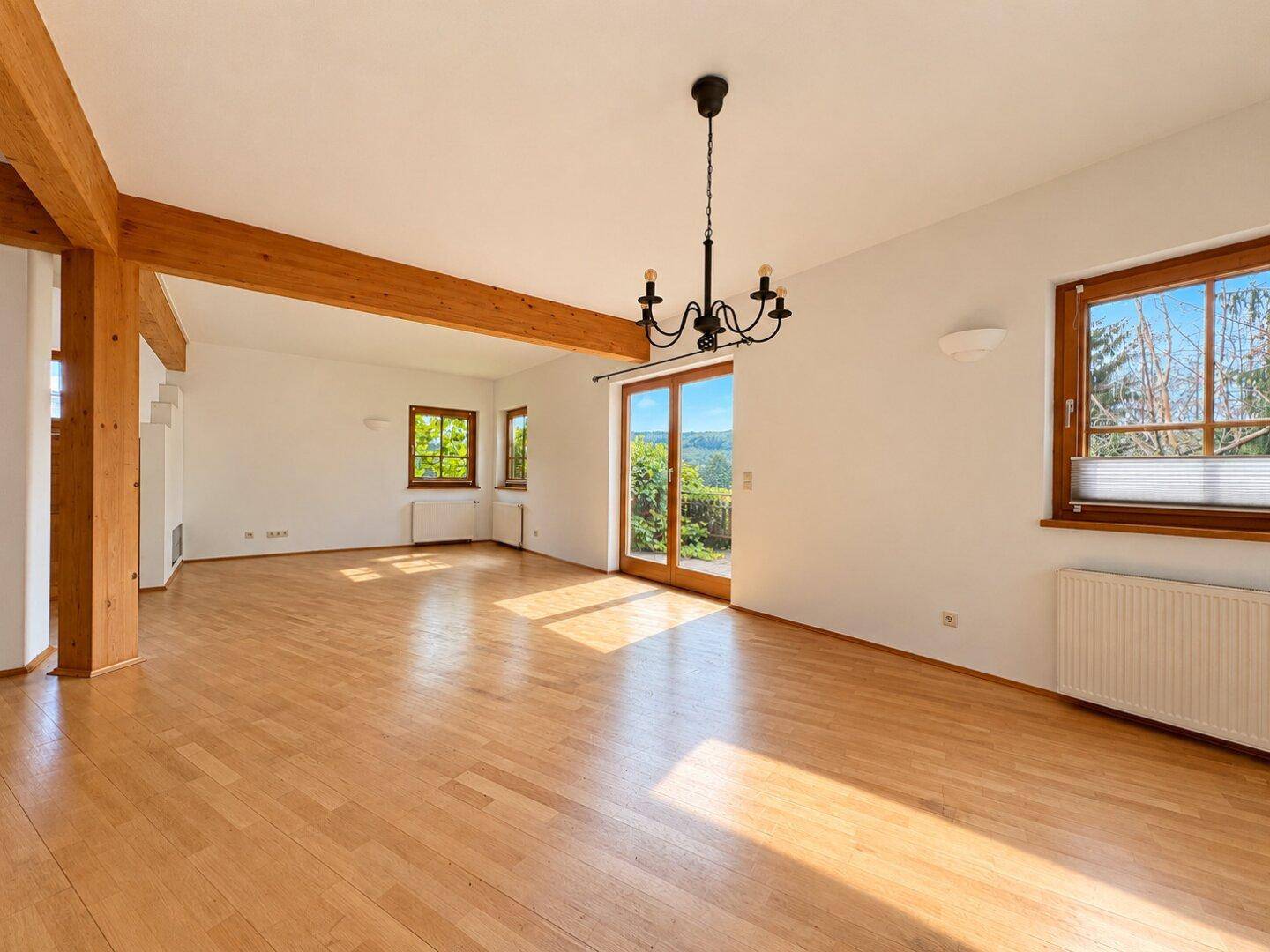 Helles, leeres Wohnzimmer mit Holzbalken, Parkettboden und Zugang zu einem Balkon.
