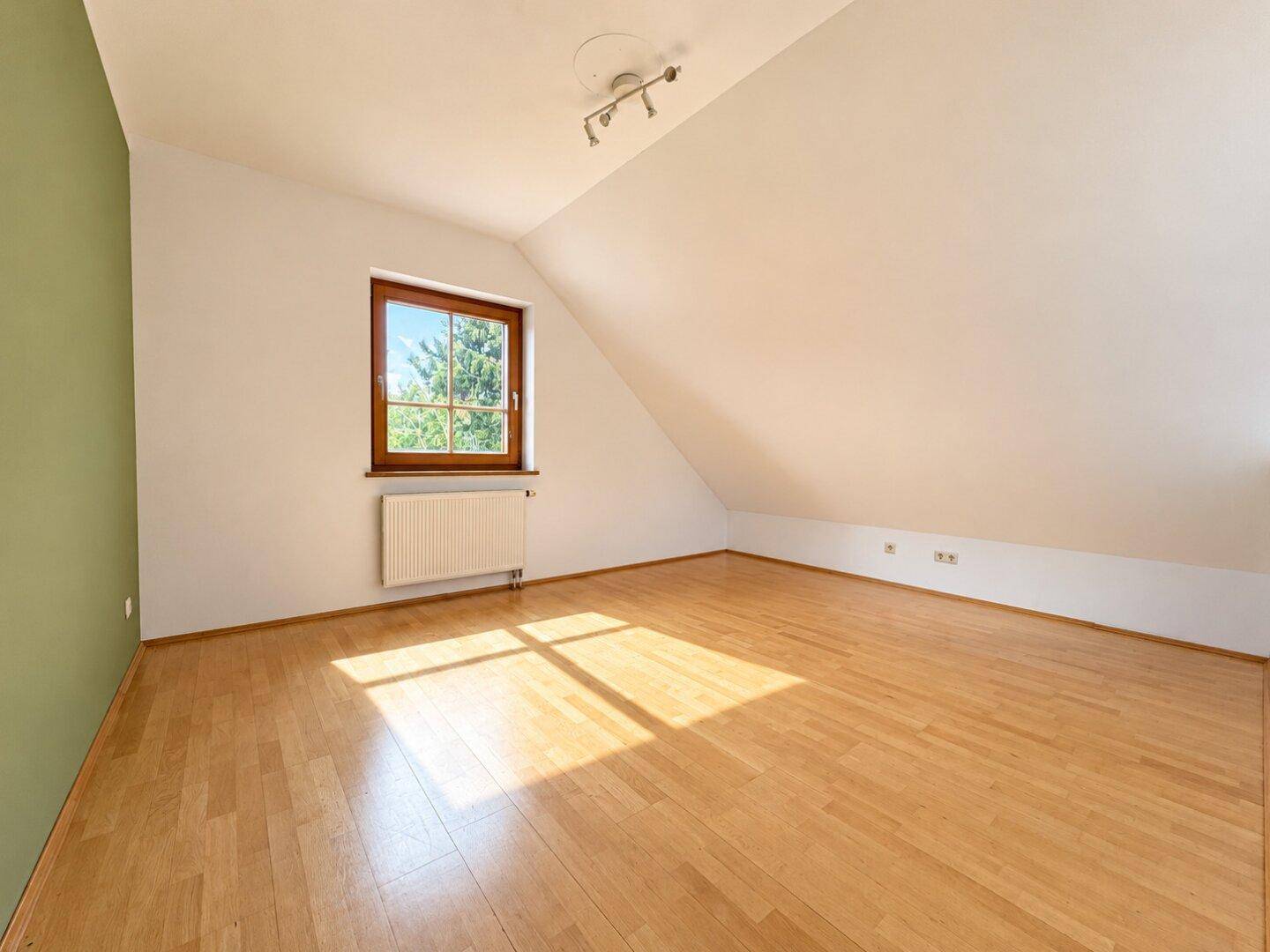 Geräumiges Schlafzimmer mit Parkettboden, Dachschräge und Fenster mit Blick ins Grüne.