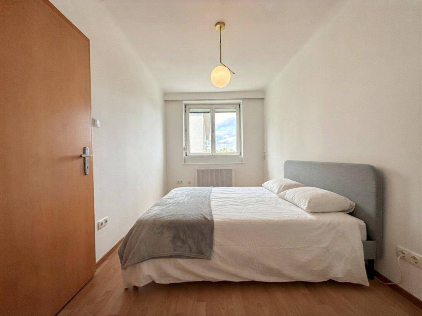 Gemütliches Schlafzimmer mit Doppelbett, Parkettboden und Fenster für natürliches Licht.