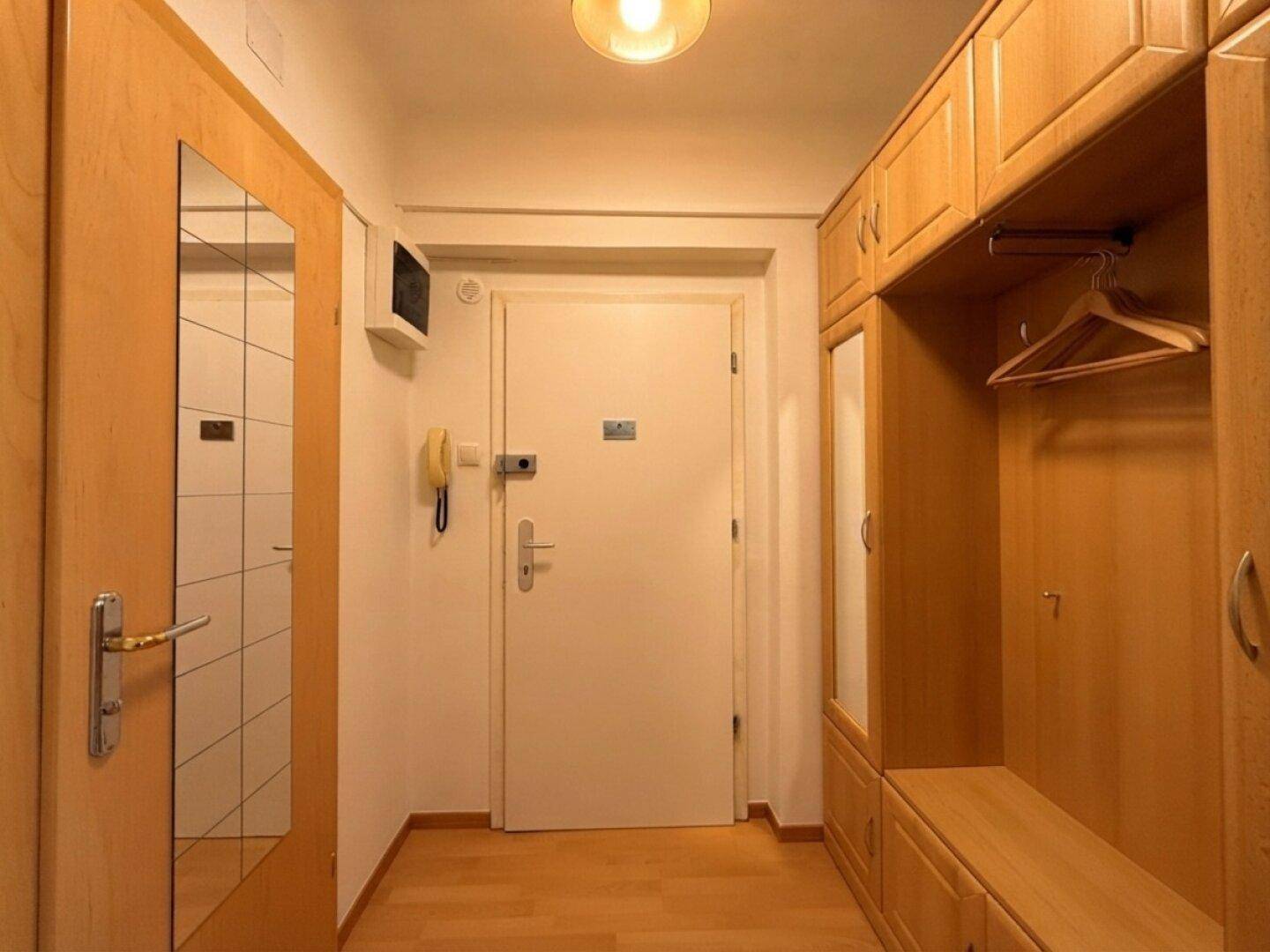 Eingangsbereich mit Holzschränken, Garderobe und Spiegel, bietet praktischen Stauraum.