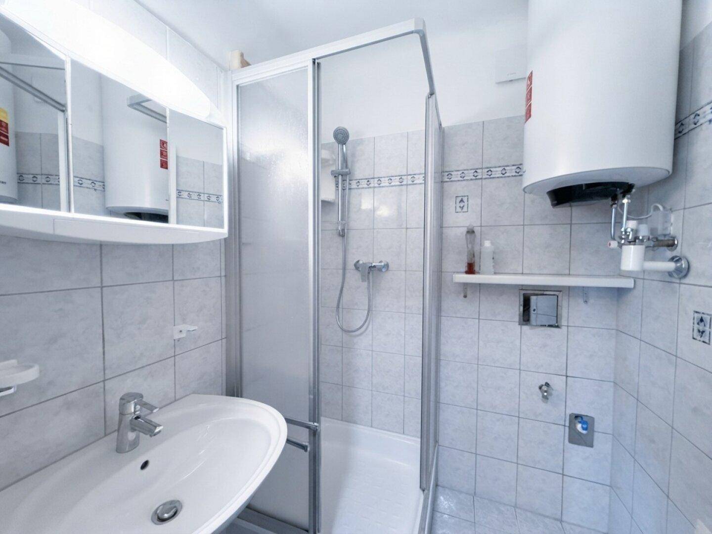 Kleines Badezimmer mit Dusche, Waschbecken und Fliesen, funktional eingerichtet.