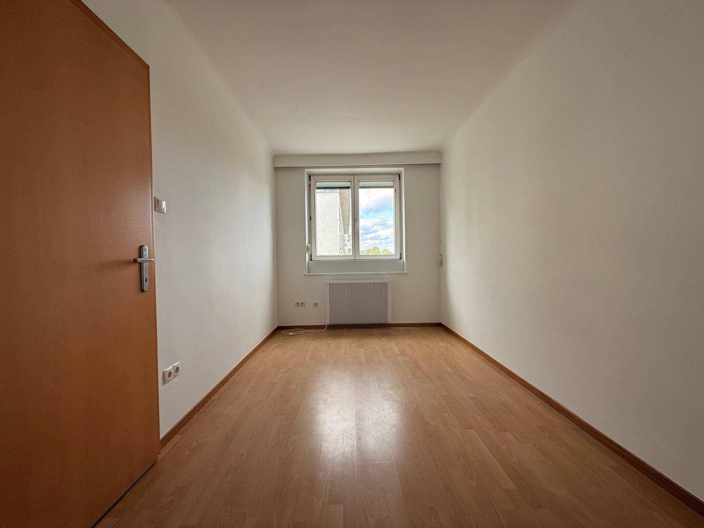 Leeres Schlafzimmer mit hellem Parkettboden und Fenster, bereit zur individuellen Gestaltung.