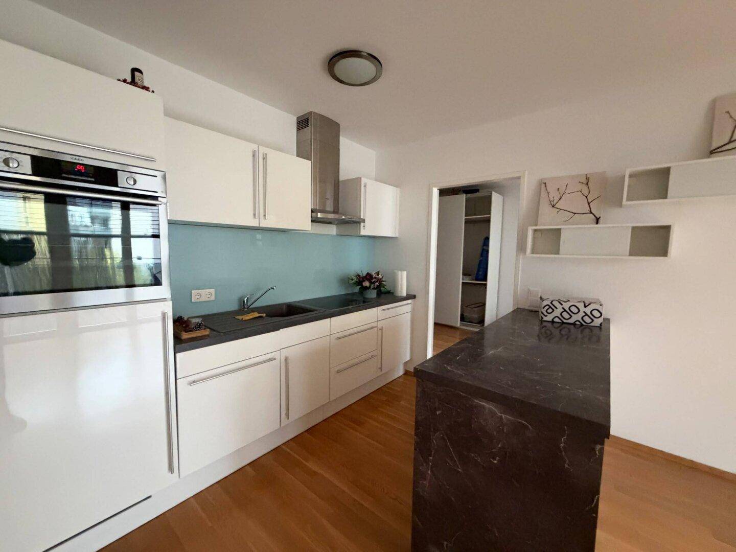 Moderne Einbauküche mit weißen Hochglanzfronten, dunkler Arbeitsplatte und integriertem Backofen.