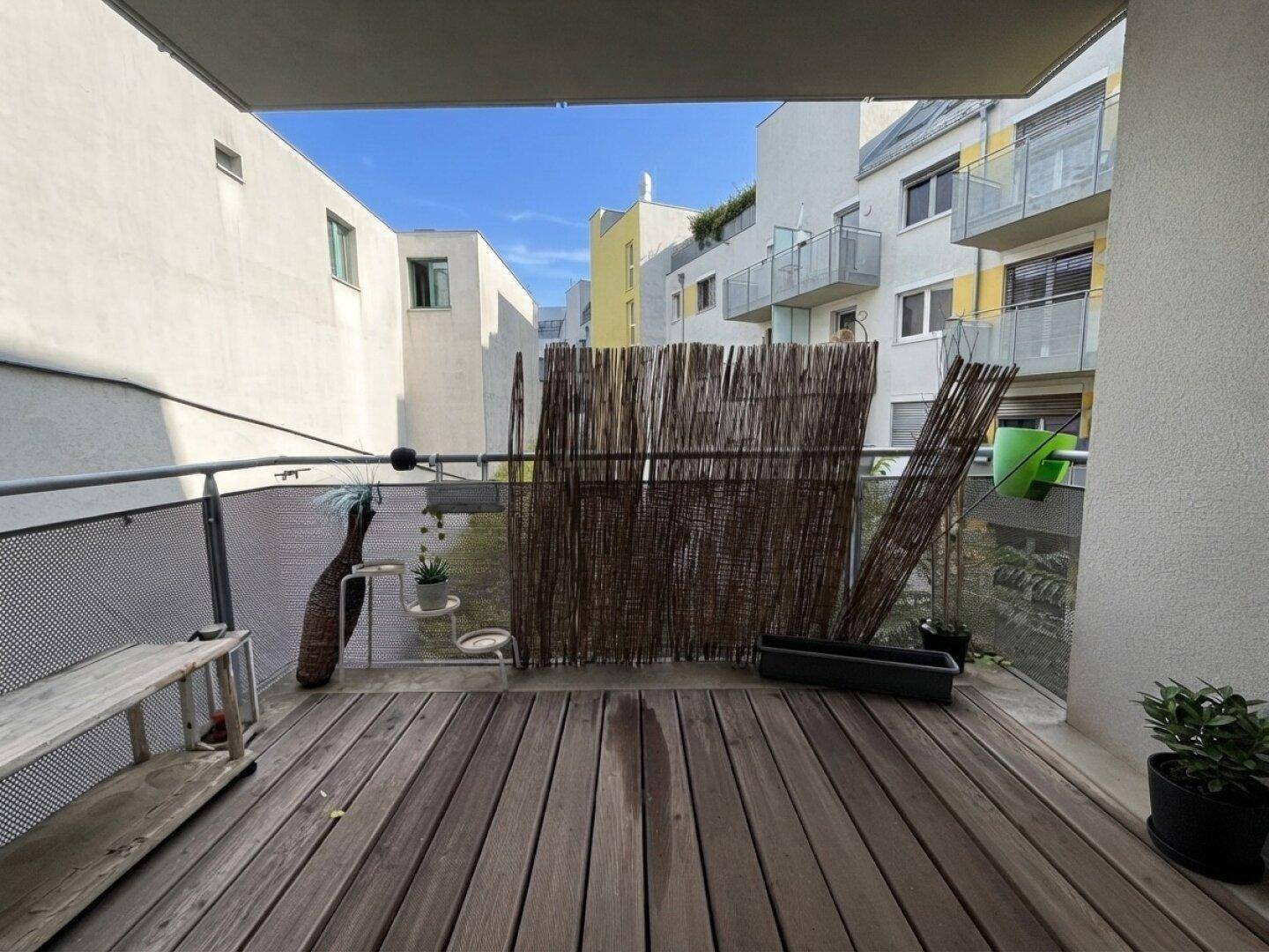 Gemütlicher Balkon mit Holzboden, Sichtschutz und Blick auf die umliegenden Gebäude.