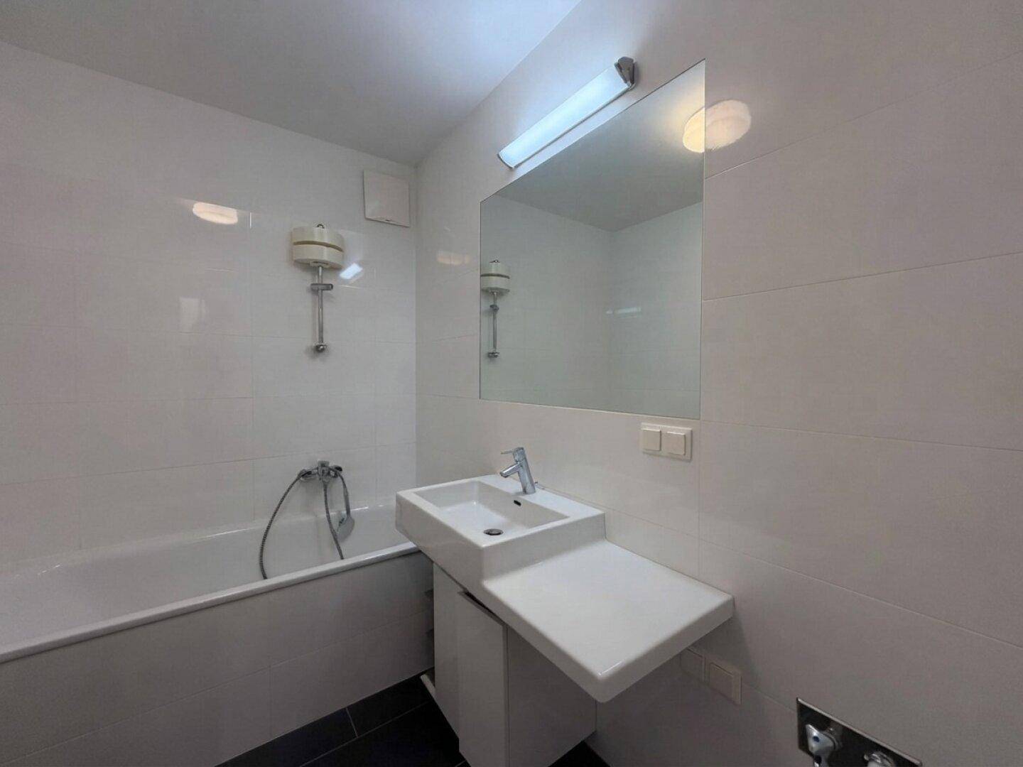 Modernes Badezimmer mit Badewanne, weiß gefliesten Wänden und einem einzelnen Waschbecken.
