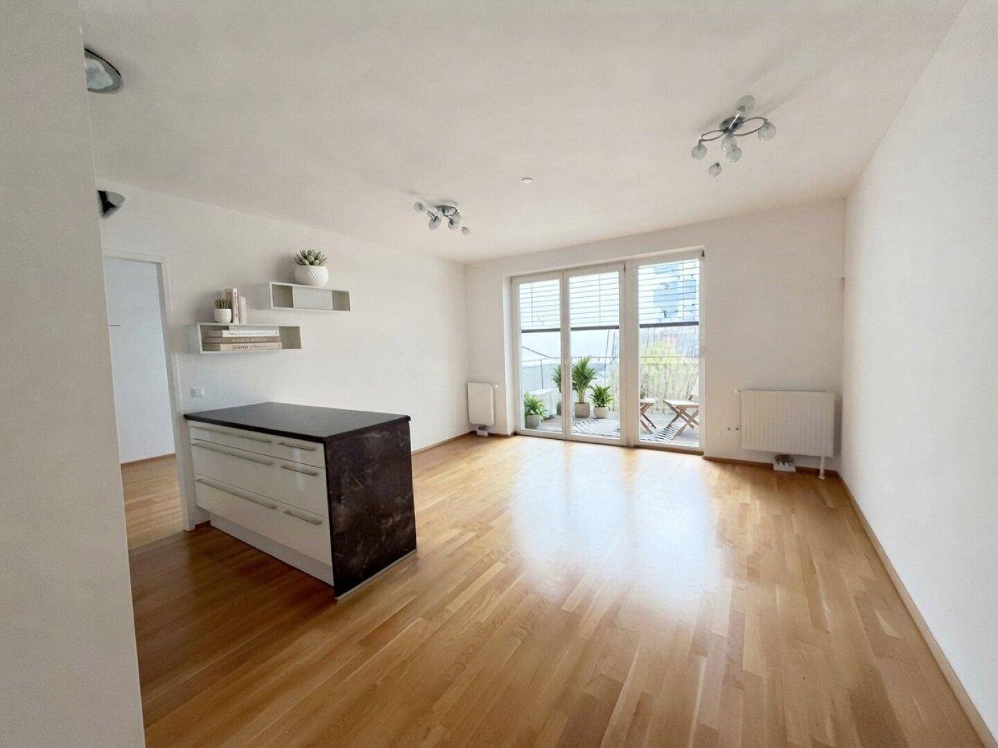Geräumiger, leerer Wohn- und Essbereich mit hellem Parkettboden und Zugang zum Balkon.