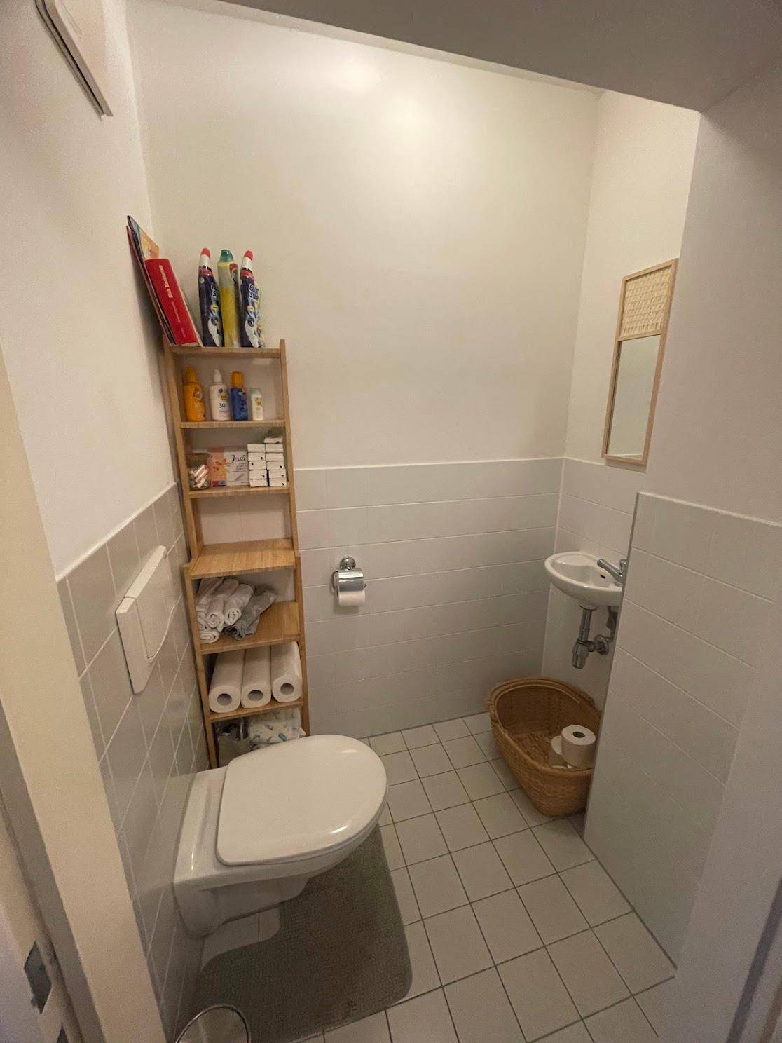 Kleines Gäste-WC mit Toilette, Waschbecken und praktischem Regal für Badartikel.