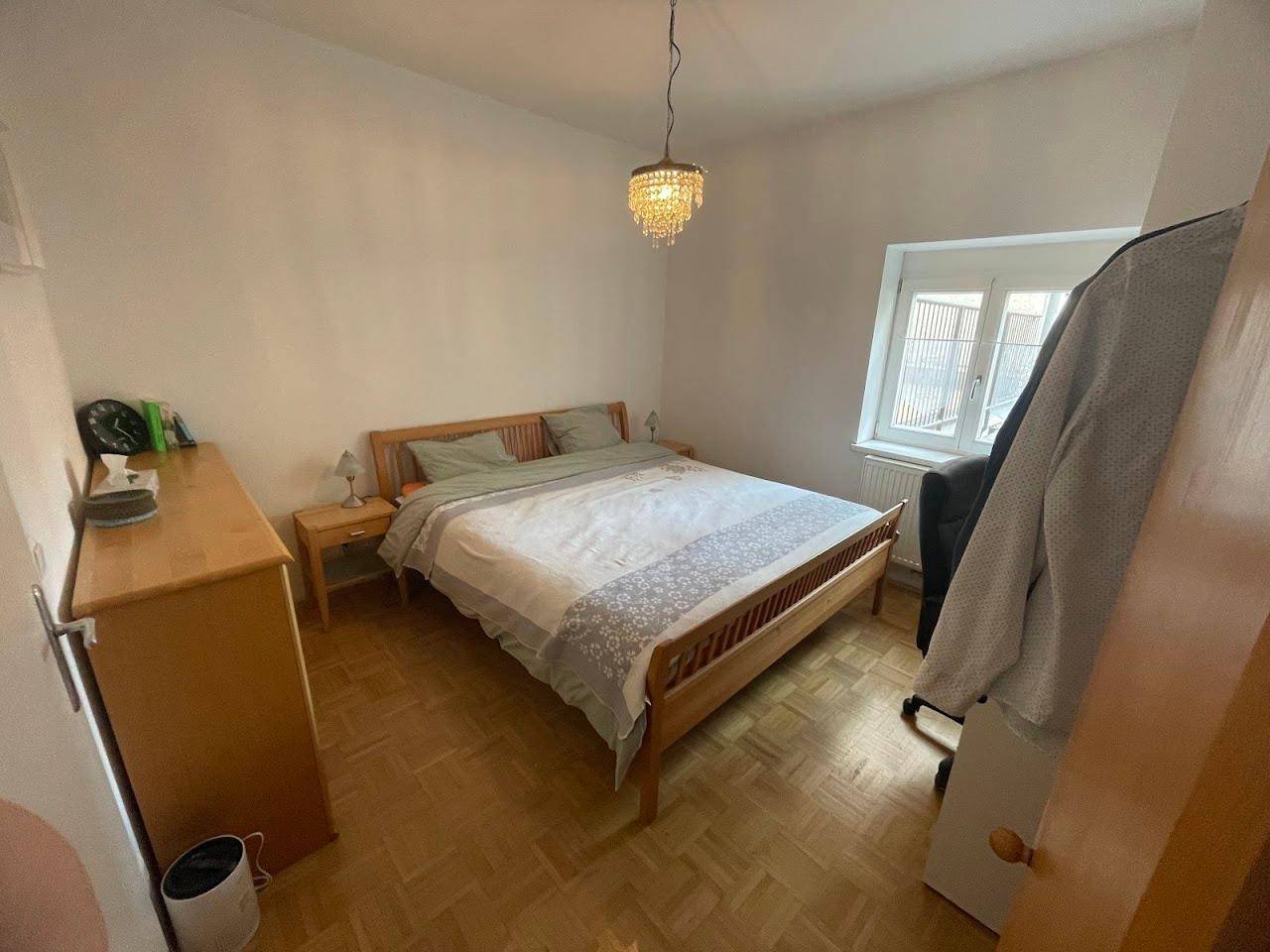 Gemütliches Schlafzimmer mit Holzbett, Nachttischen und Kommode, beleuchtet von einem Kronleuchter.