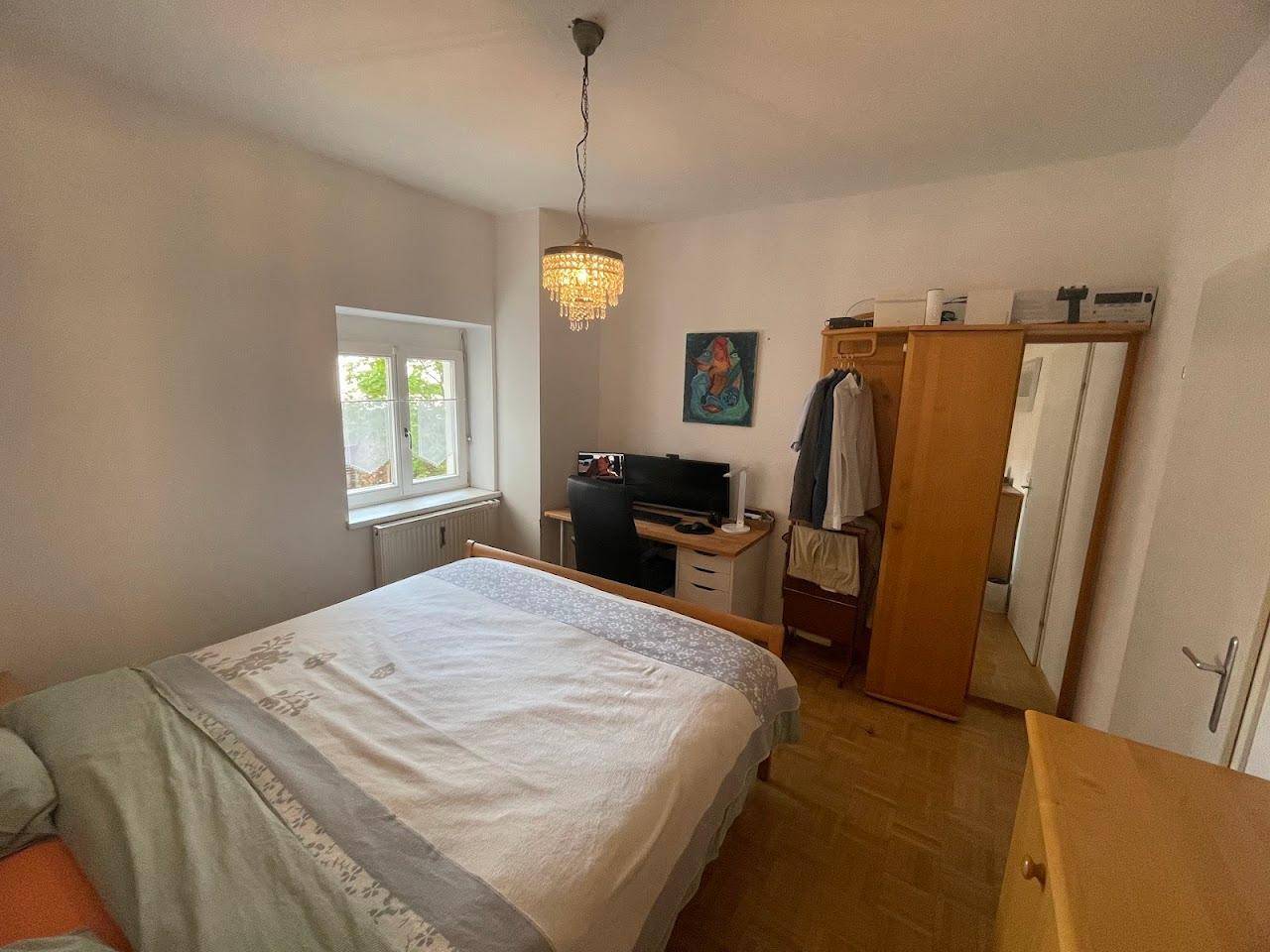 Helles Schlafzimmer mit Holzbett, Schreibtisch und Kleiderschrank, ausgestattet mit Parkettboden.