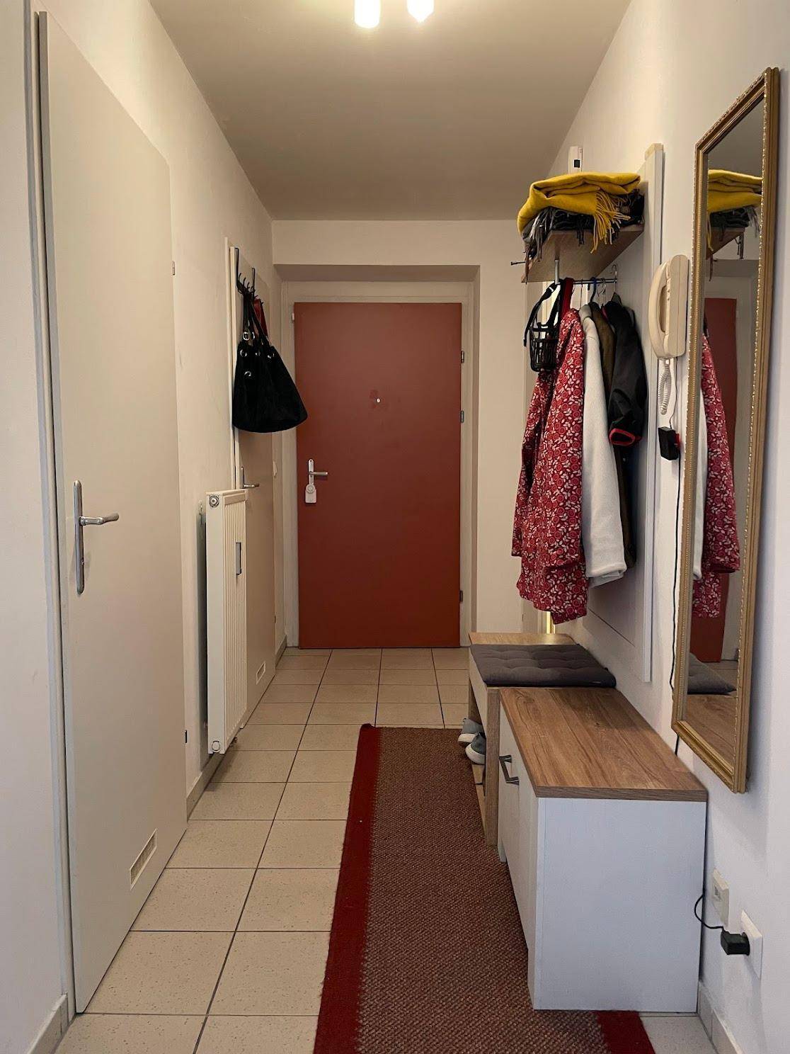 Heller Eingangsbereich mit Garderobe, Spiegel und Fliesenboden, der zum Wohnbereich führt.